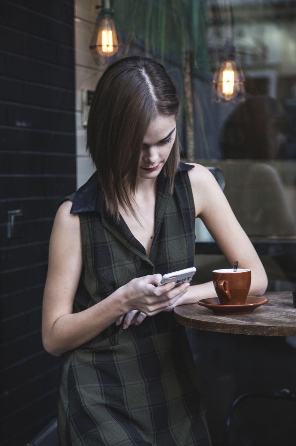 Free Image of Woman Sitting at Table Looking at Cell Phone 
