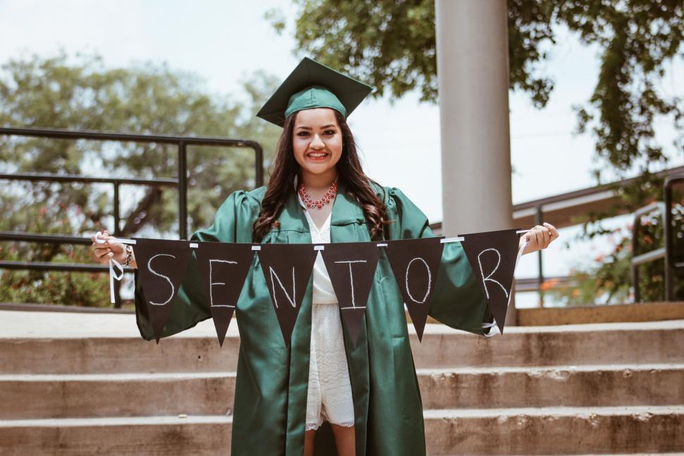 Free Image of Woman in Graduation Gown Holding Senior Sign 