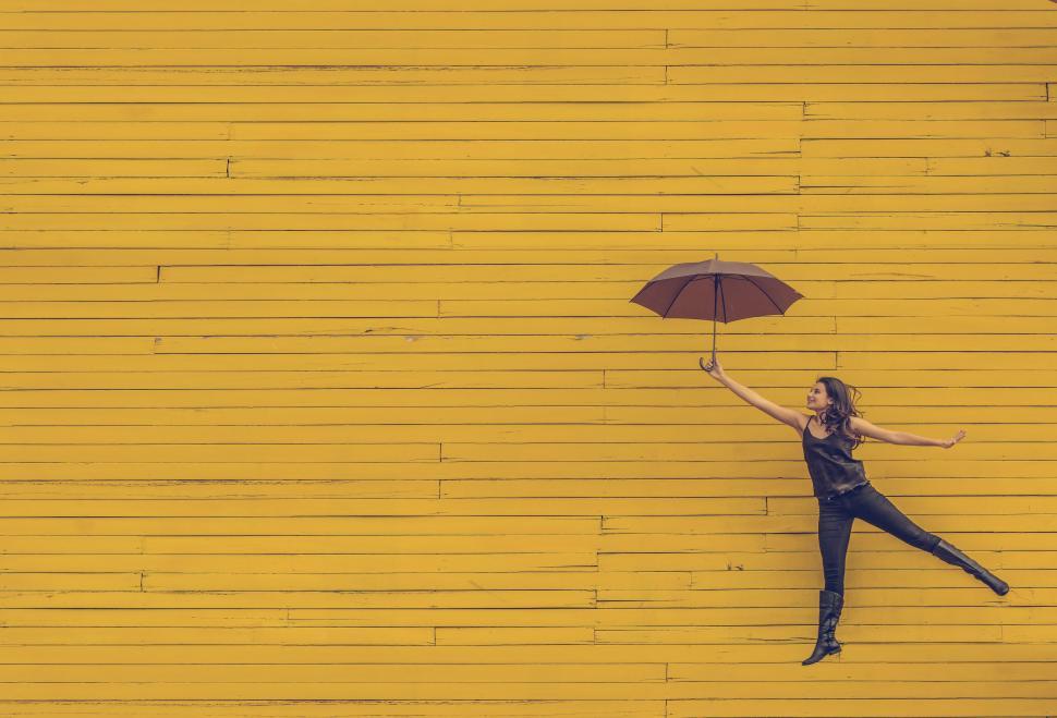 Free Image of Woman Holding Umbrella in Front of Yellow Wall 