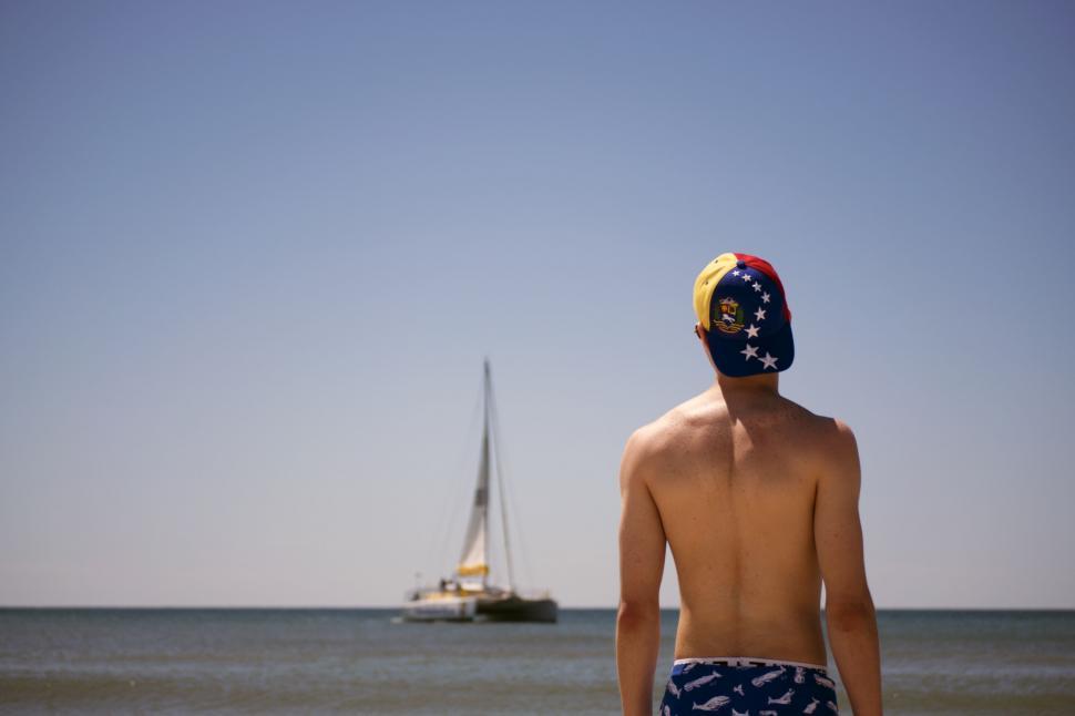 Free Image of Man Standing on Beach With Boat in Background 