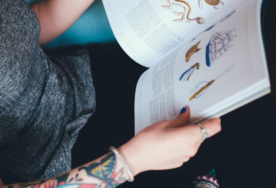 Free Image of Woman Reading Book With Arm Tattoos 