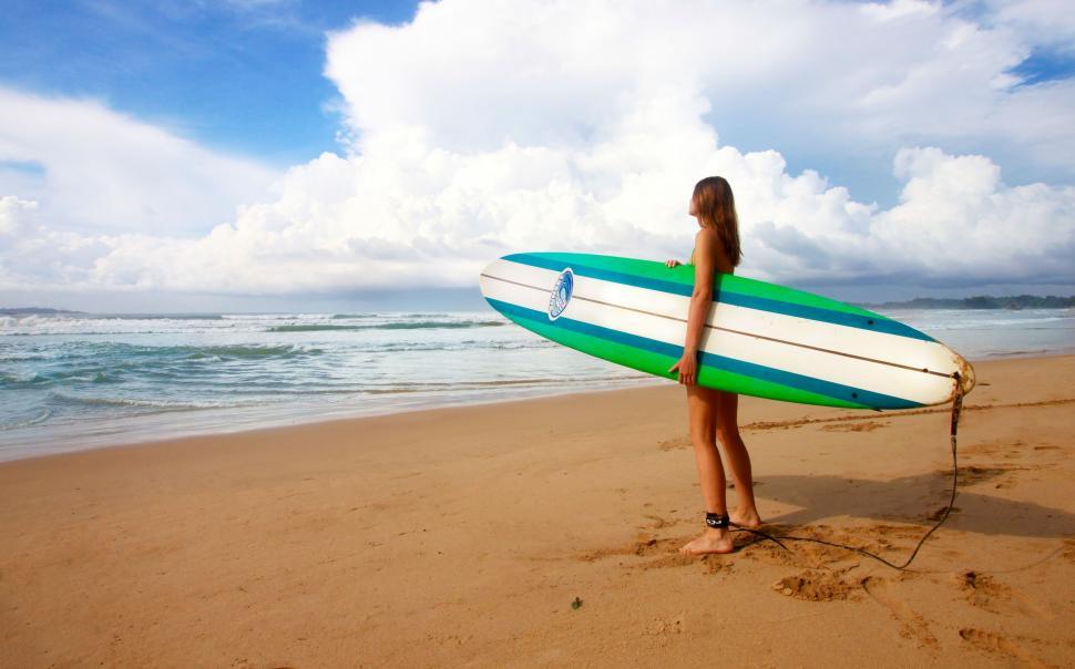 Free Image of Woman Standing on Beach Holding Surfboard 