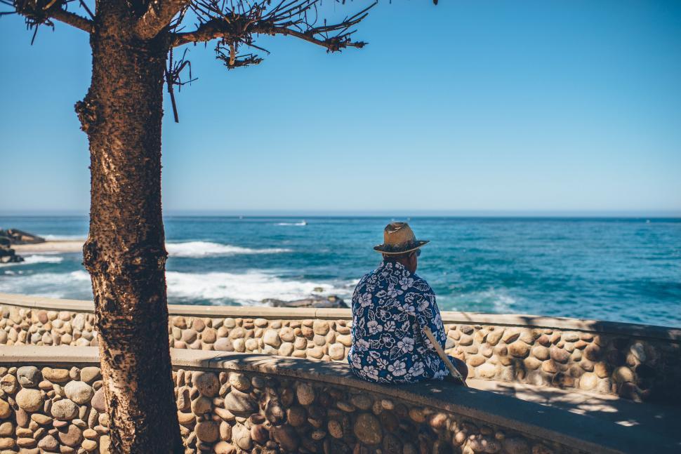 Free Image of Person Sitting on Stone Wall Overlooking Ocean 