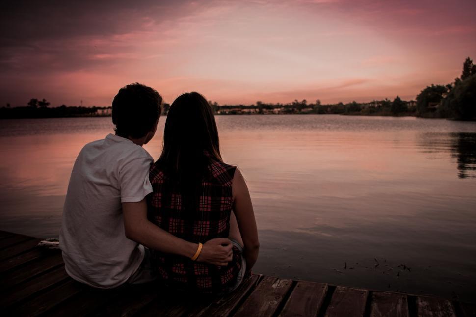 Free Image of Man and Woman Sitting on Dock by Water 