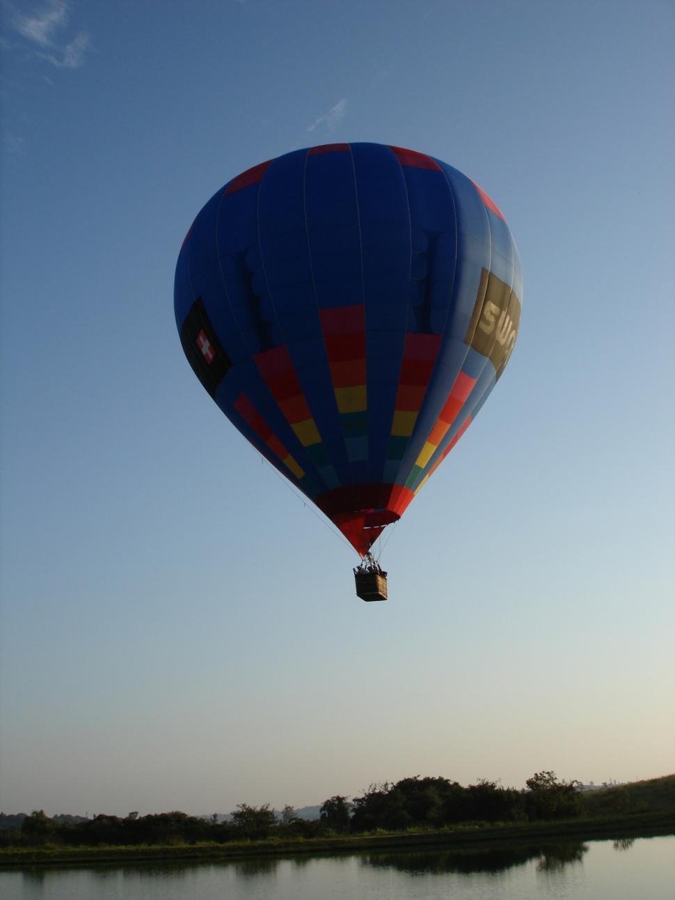 Free Image of Blue and Red Hot Air Balloon Flying Over a Lake 