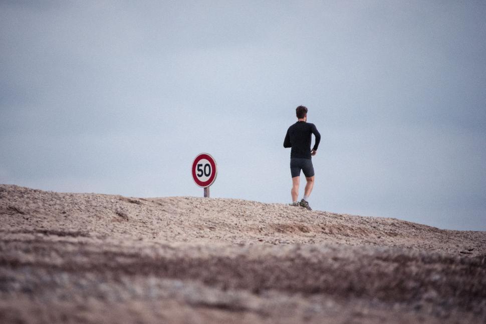 Free Image of Man Standing on Sandy Hill Next to Speed Limit Sign 