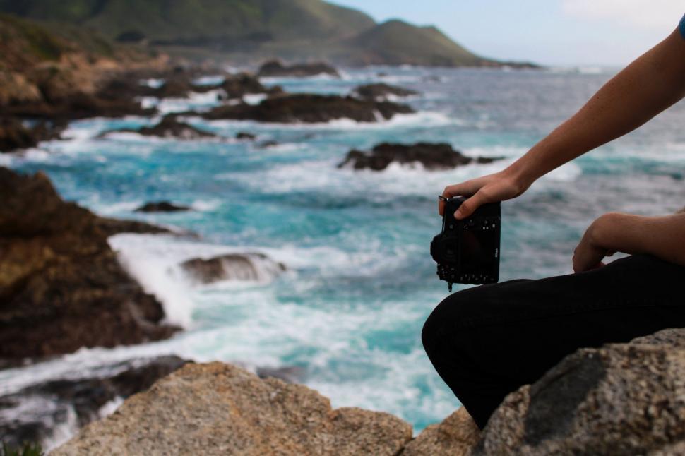 Free Image of Person Sitting on Rock Taking Picture of Ocean 