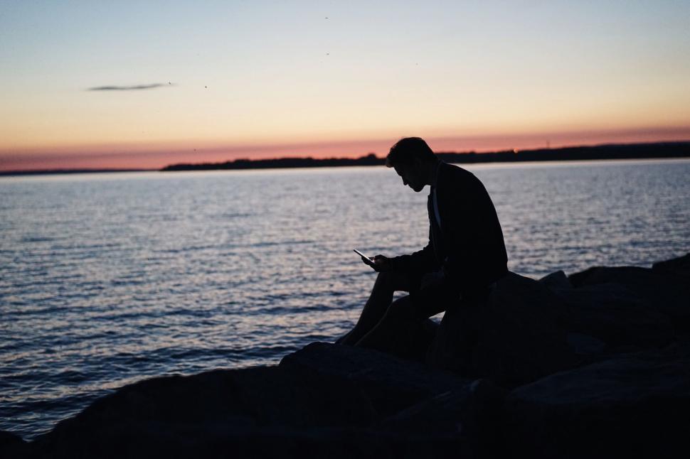 Free Image of Man Sitting on Rock Using Cell Phone 