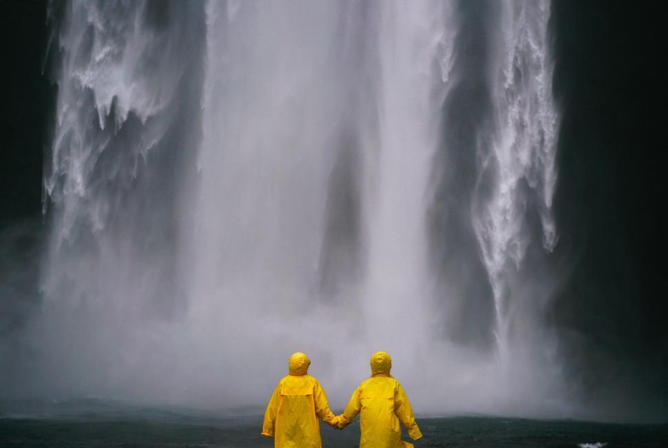 Free Image of Two People in Yellow Raincoats Standing in Front of a Waterfall 