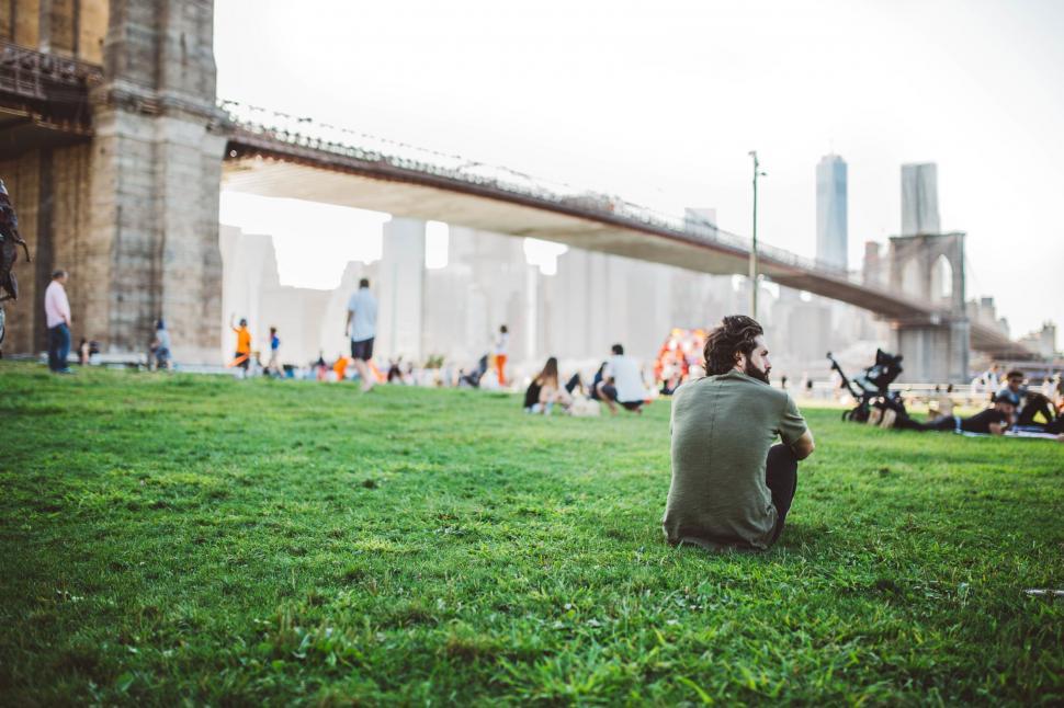 Free Image of Man Sitting on Grass in Front of Bridge 