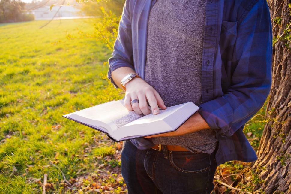 Free Image of Man Standing by Tree Holding Book 