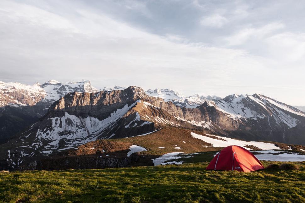 Free Image of Tent Pitched Up on Grassy Hill With Mountains in Background 