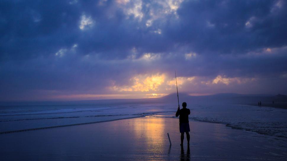 Free Image of Man Standing on Beach Holding Fishing Pole 