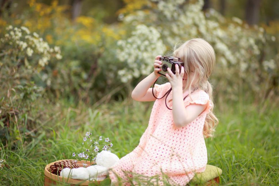 Free Image of Little Girl Sitting in Grass With Camera 