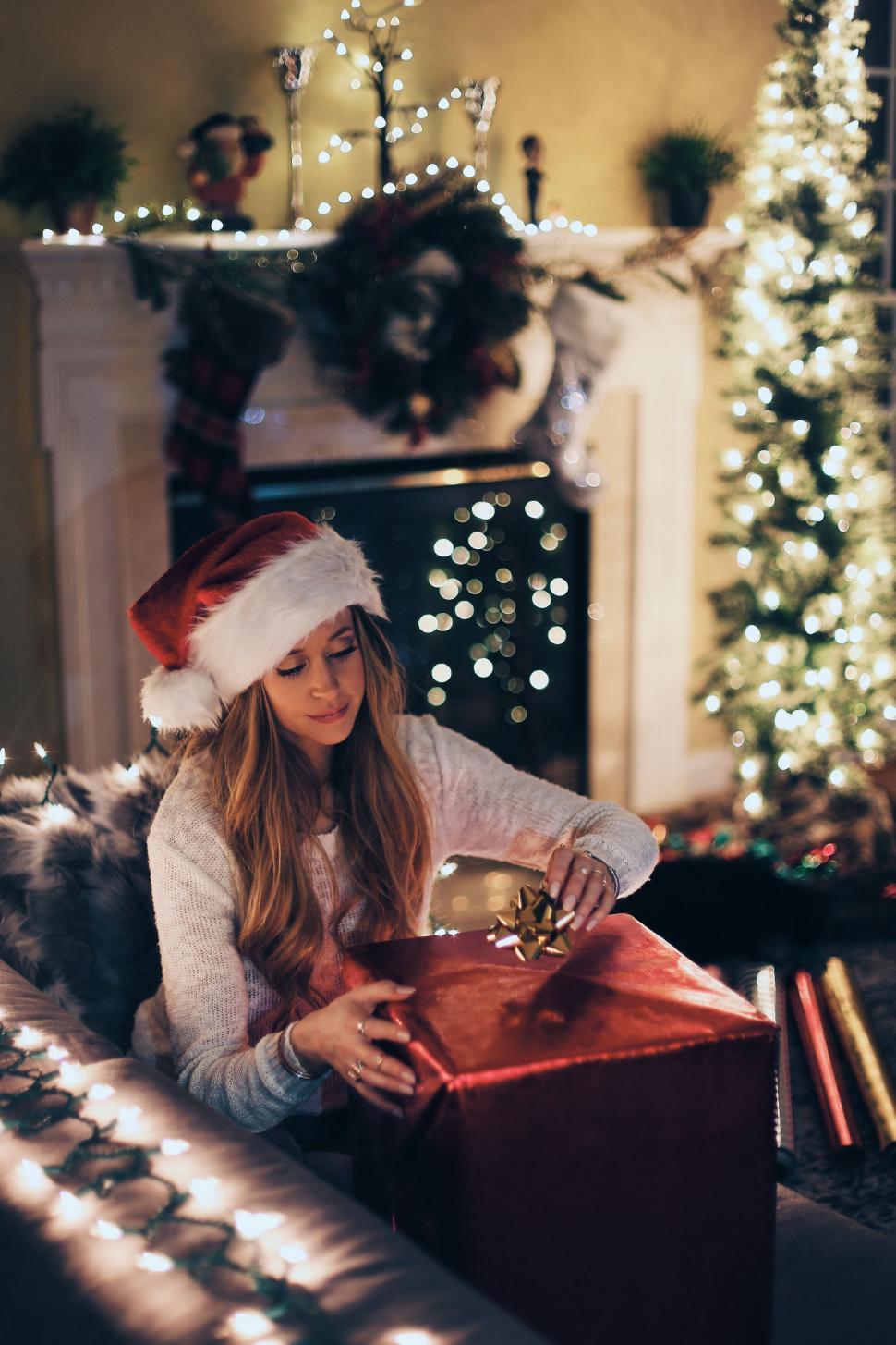 Free Image of Woman in Santa Hat Opening Christmas Present 