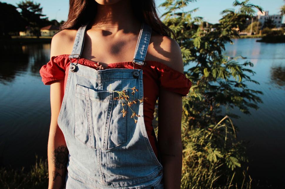 Free Image of Woman Wearing Denim Overalls Standing by Lake 