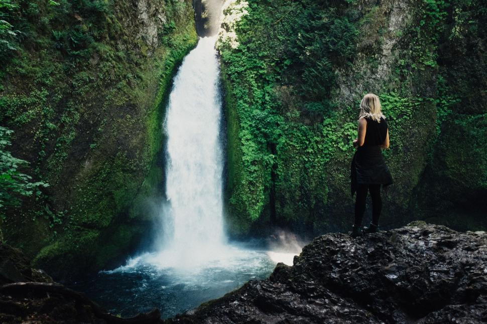 Free Image of Woman Standing on Cliff Looking at Waterfall 