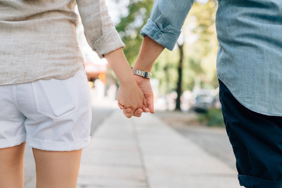 Free Image of Two People Holding Hands Walking Down a Sidewalk 