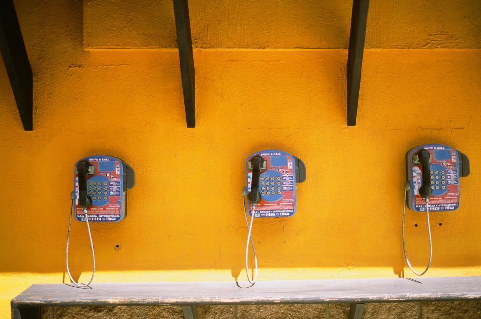 Free Image of Row of Old Style Telephones Mounted to Yellow Wall 