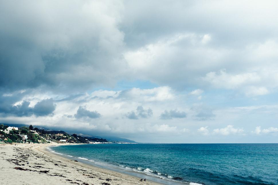 Free Image of Sandy Beach by Ocean Under Cloudy Sky 