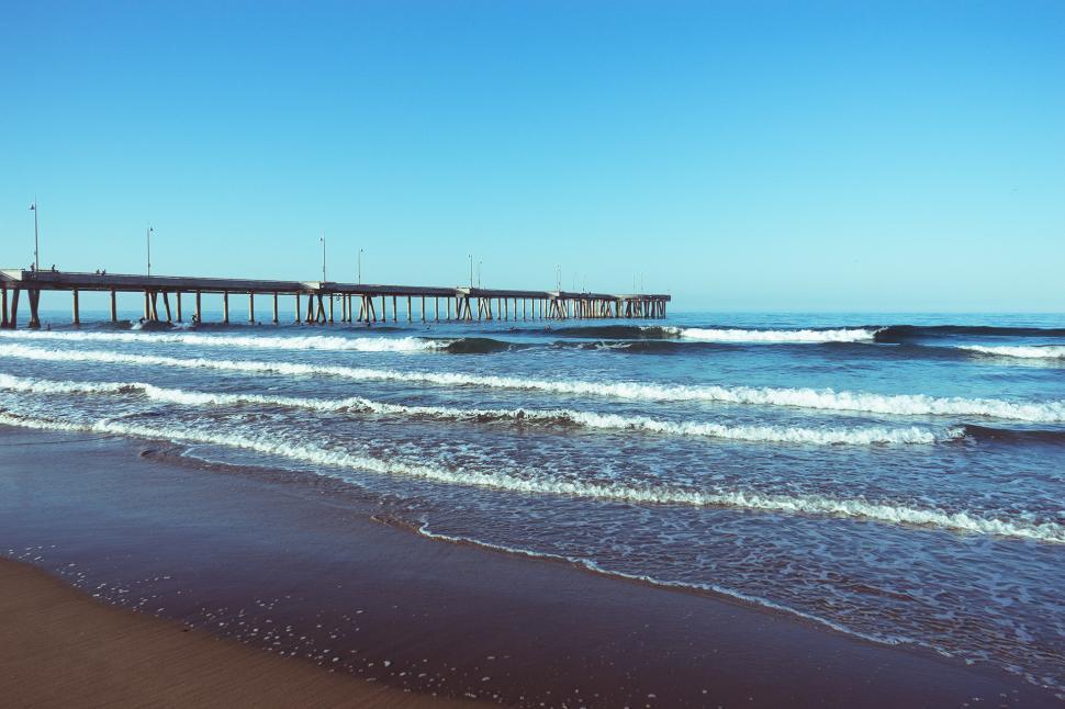 Free Image of Beach With Waves and Pier in Background 