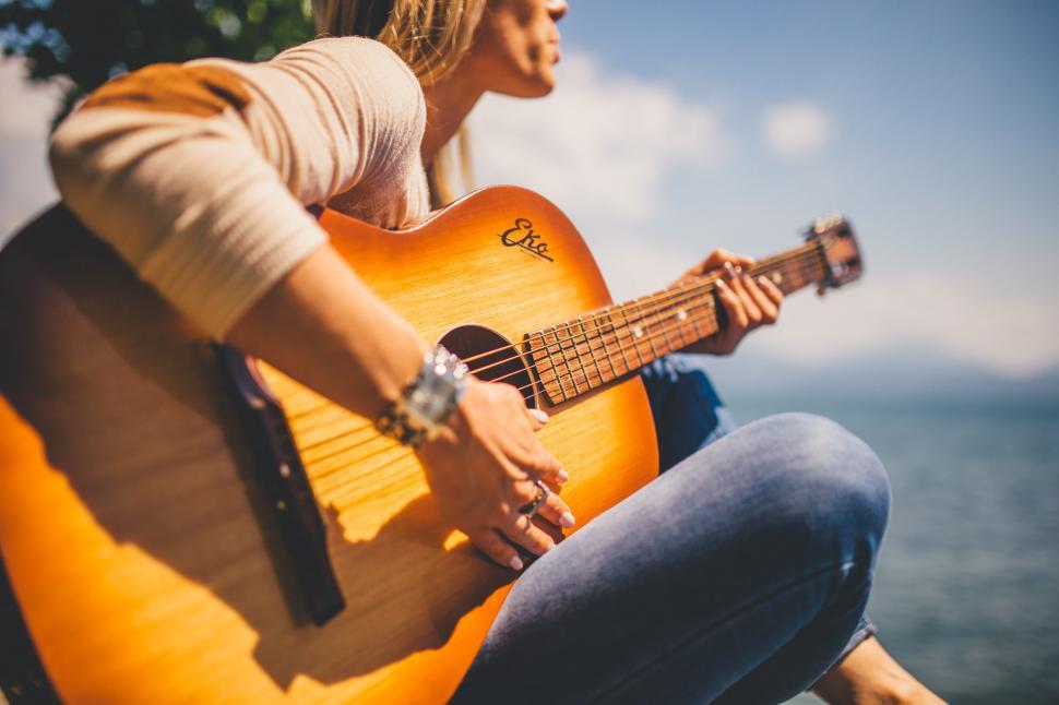 Free Image of Woman Sitting on Rock Playing Guitar 