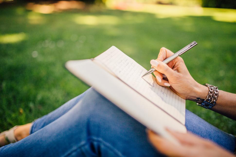 Free Image of Person Sitting in Grass Writing on a Notebook 