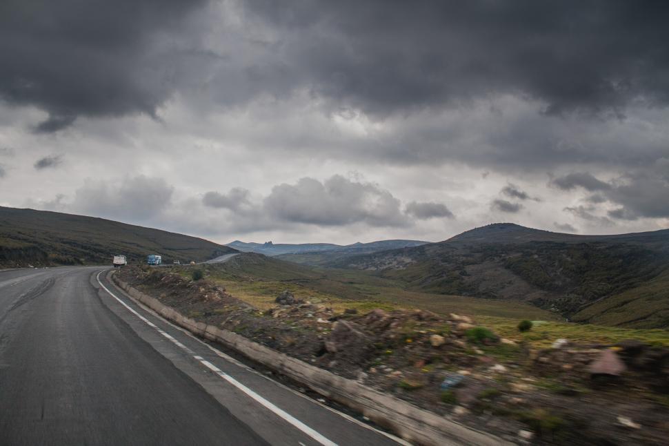 Free Image of Car Driving Down Road Under Cloudy Sky 