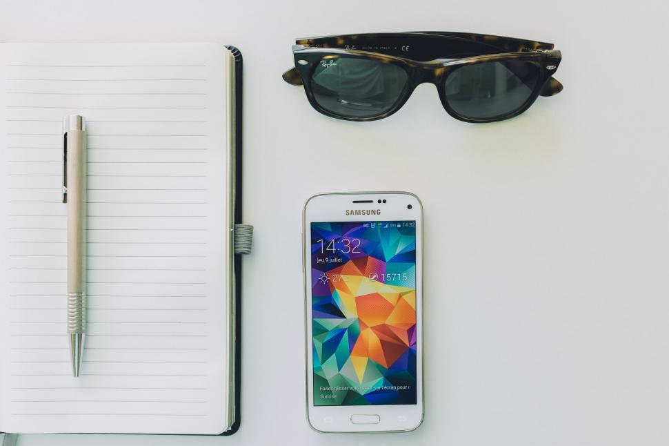Free Image of Office Desk Essentials: Notepad, Pen, Sunglasses, Cell Phone 