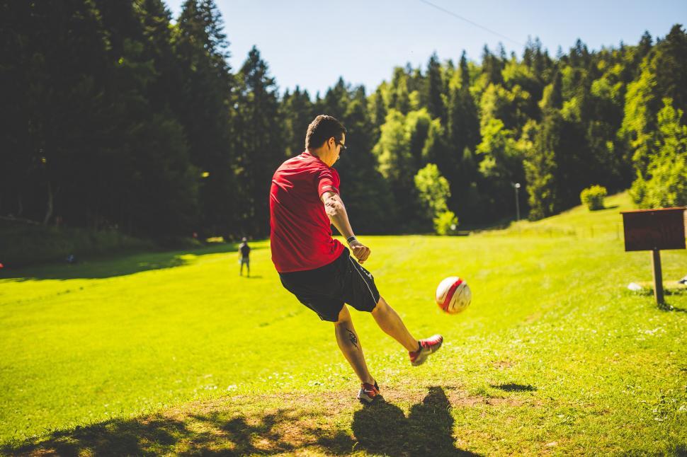 Free Image of Man Kicking Soccer Ball Across Lush Green Field 