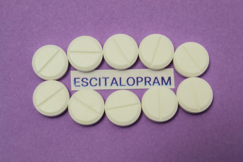Free Image of White tablet with dividing strip lie around clearly printed on paper of generic name of the drug or medication escitalopram on purple background  