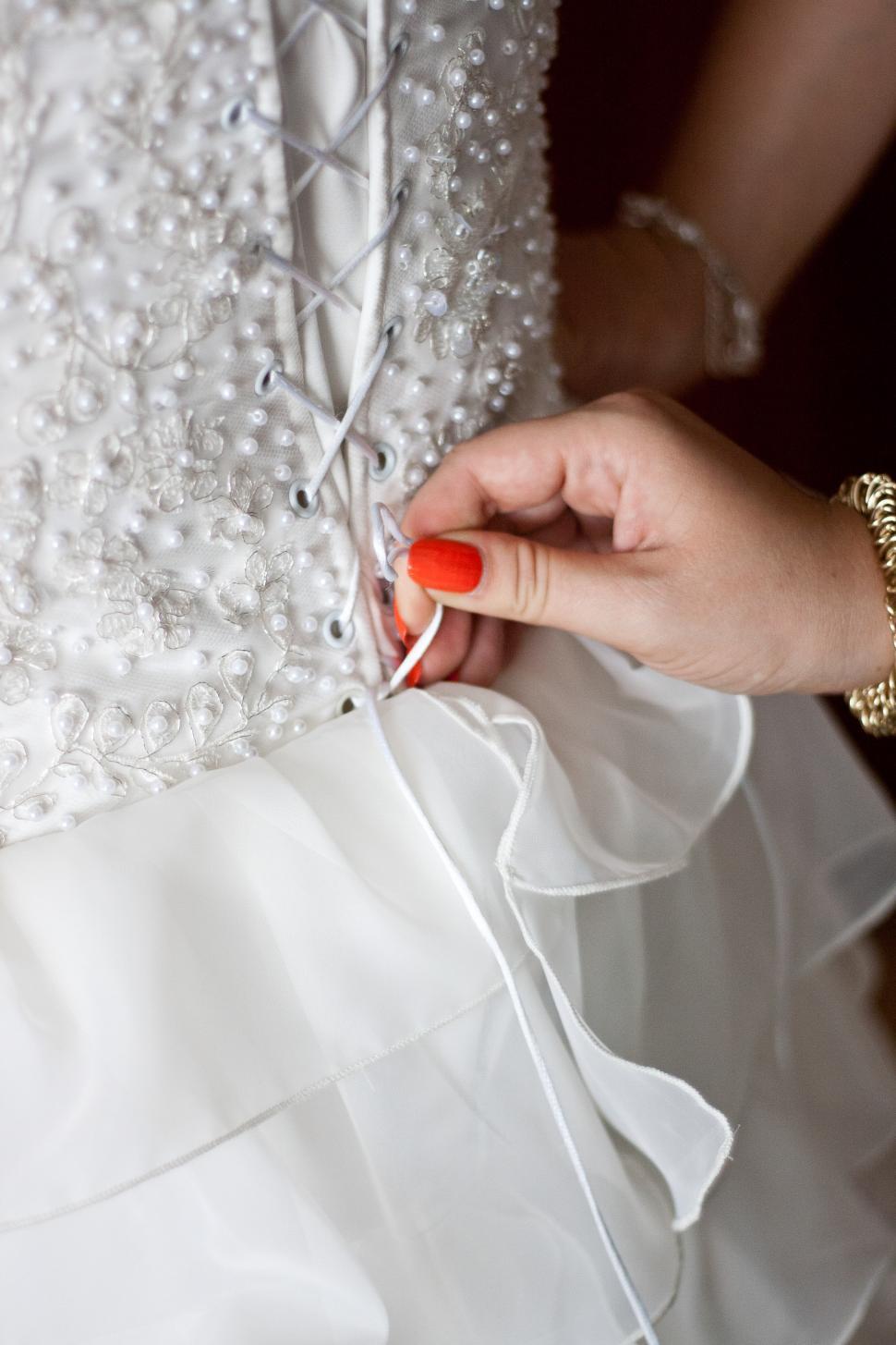 Free Image of Woman in White Dress Tying Wedding Dress 