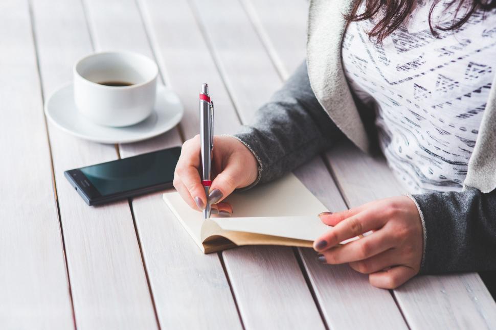 Free Image of Woman Writing on Piece of Paper Beside Cup of Coffee 