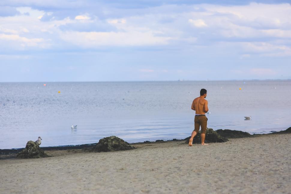 Free Image of Man Standing on Sandy Beach Next to Ocean 