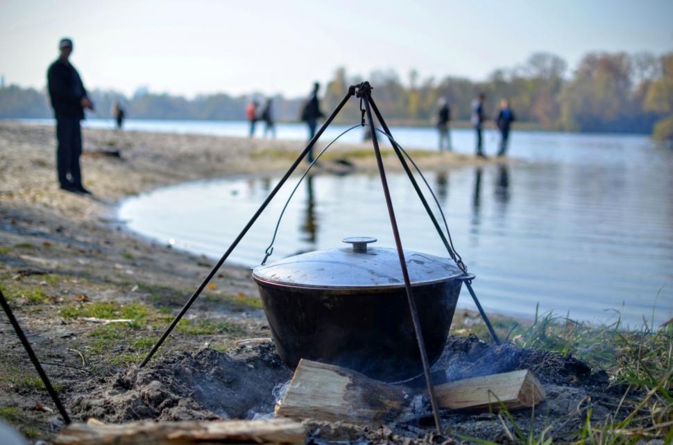Free Image of Cooking food in nature against the backdrop of the river with fishermen  