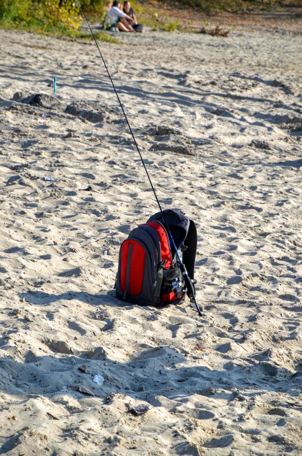 Free Image of Fisherman's bag with spinning rod lies on the sand on the shore of the river  