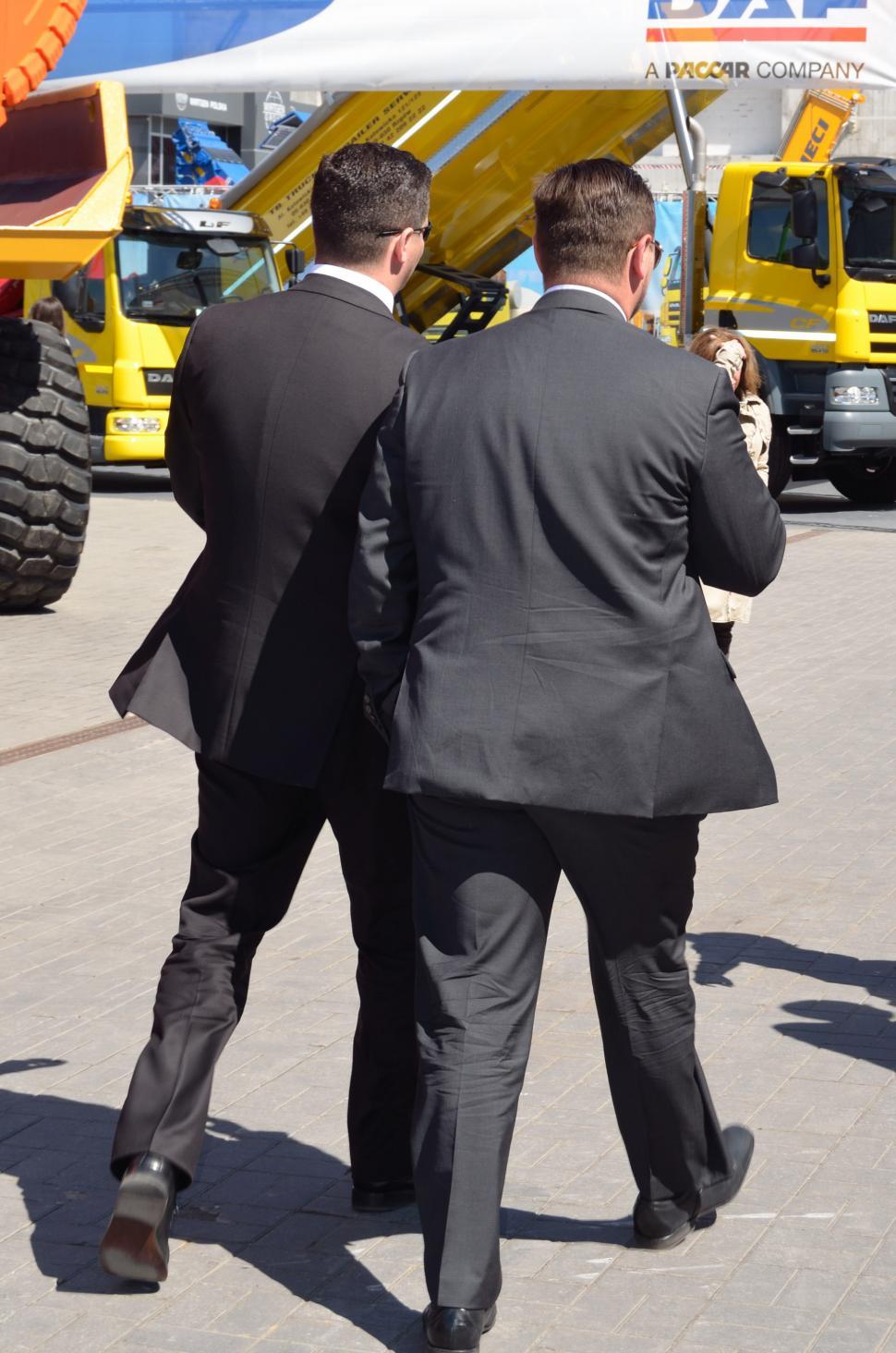 Free Image of Two Men in Suits Walking Towards a Yellow Truck 
