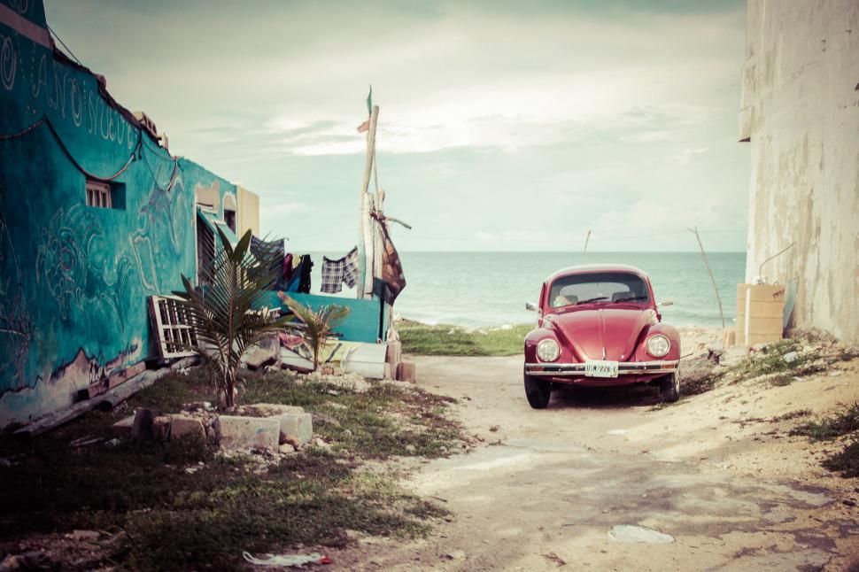 Free Image of Red Car Parked on Dirt Road by Ocean 