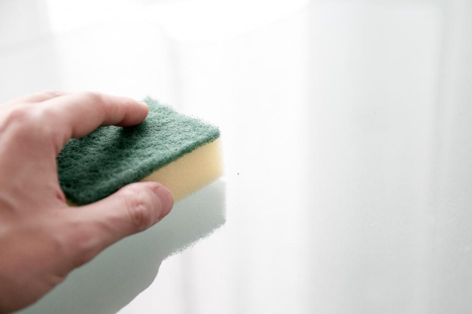 Free Image of Person Holding a Sponge on a Window Sill 