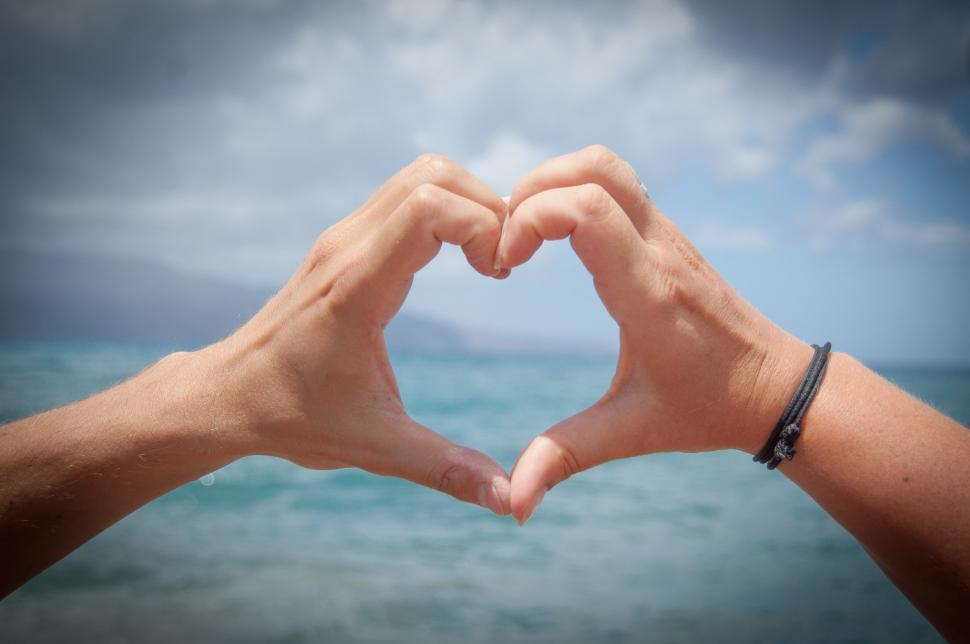 Free Image of Two Hands Forming Heart Shape With Ocean Background 