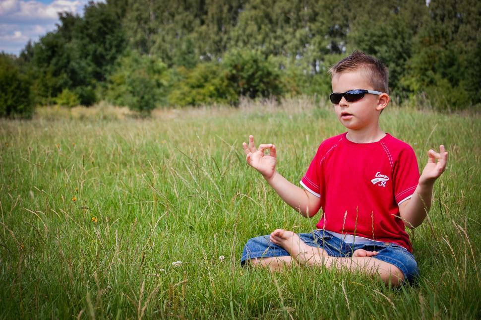 Free Image of Young Boy Sitting in Field With Hands Raised 
