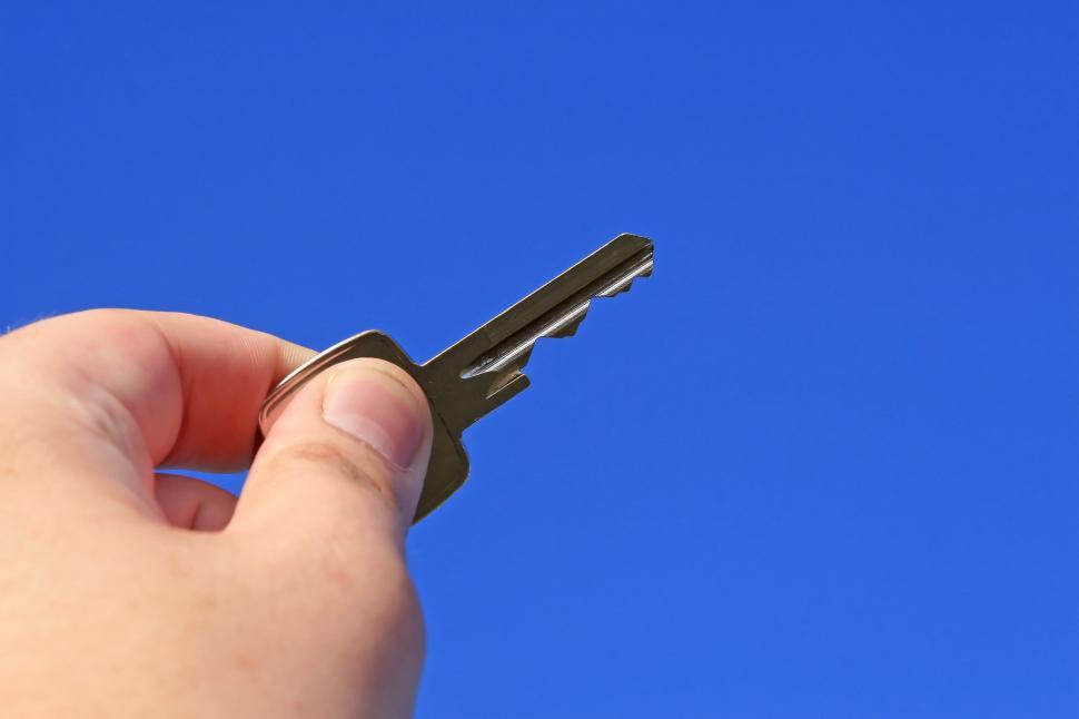 Free Image of Hand Holding Small Black Object Against Blue Sky 