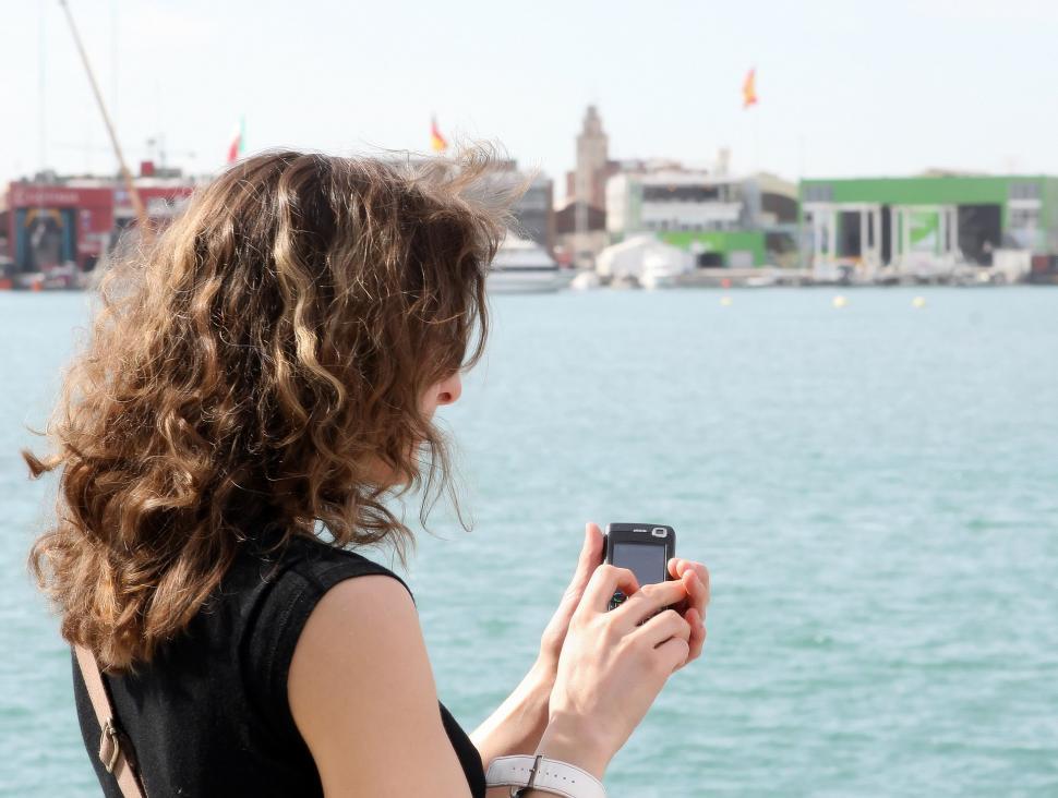 Free Image of Woman Looking at Cell Phone by Waterfront 