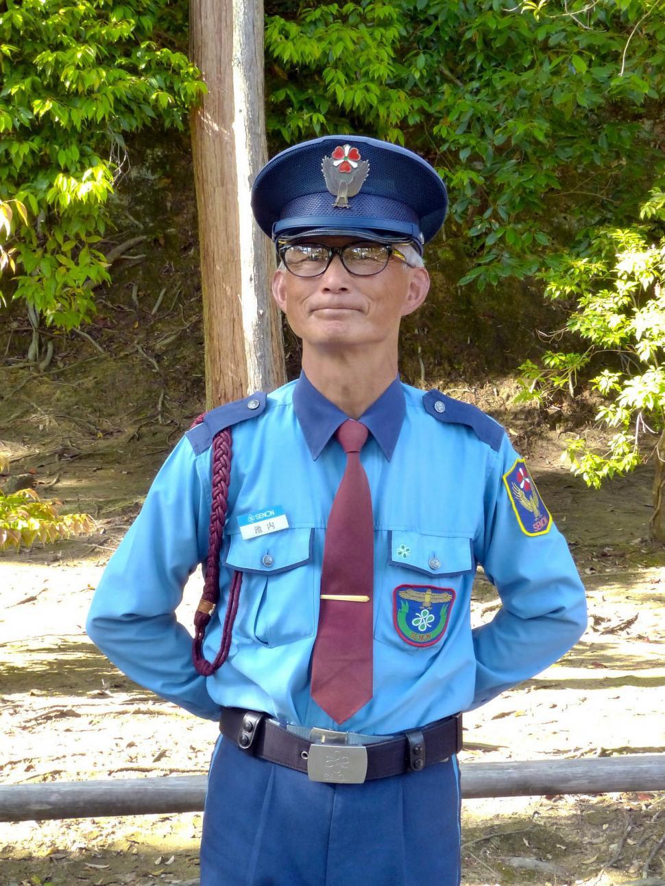 Free Image of Man in Blue Uniform Standing in Front of Fence 