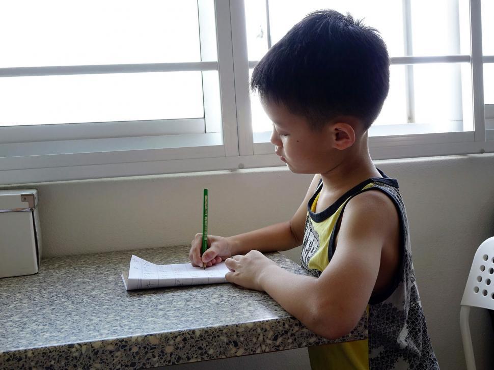 Free Image of Young Boy Sitting at Counter Writing on Piece of Paper 