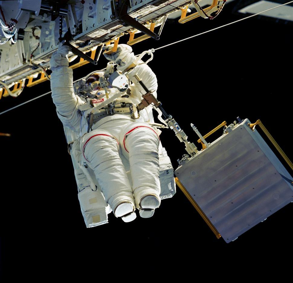 Free Image of Man in White Spacesuit Hanging From Side of Space Station 