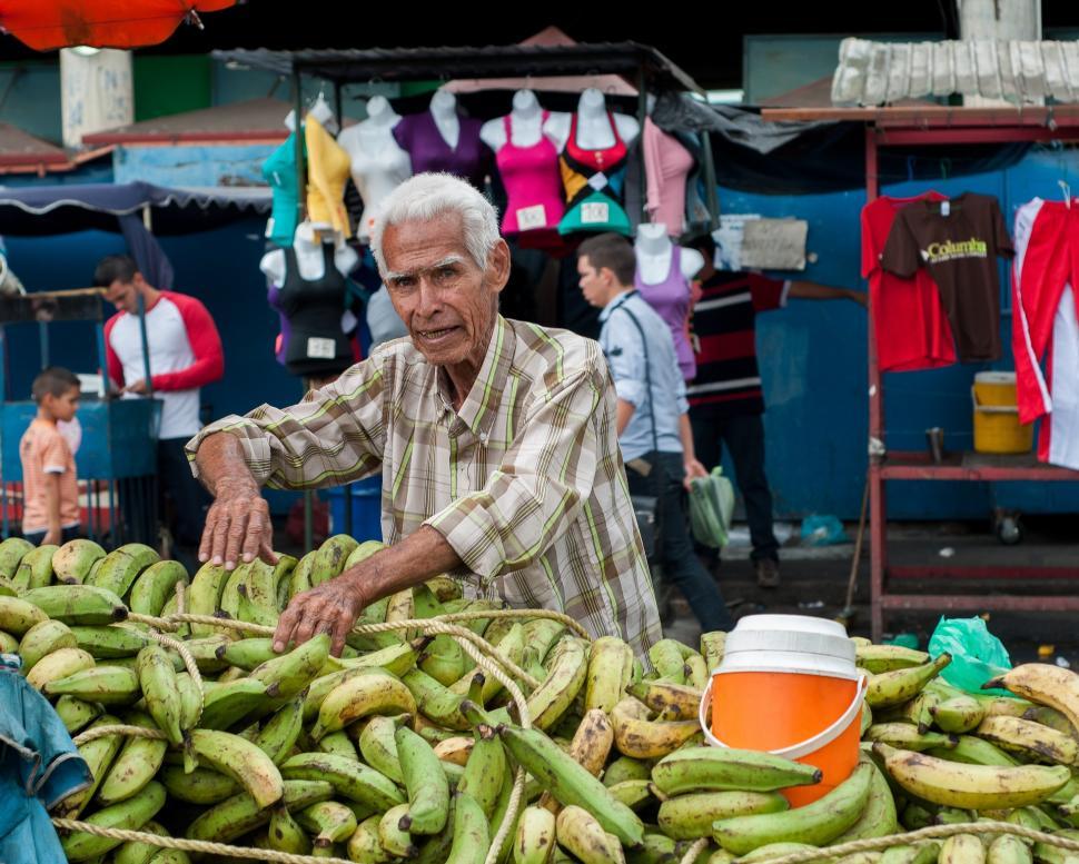 Free Image of Man Standing Next to Pile of Green Bananas 