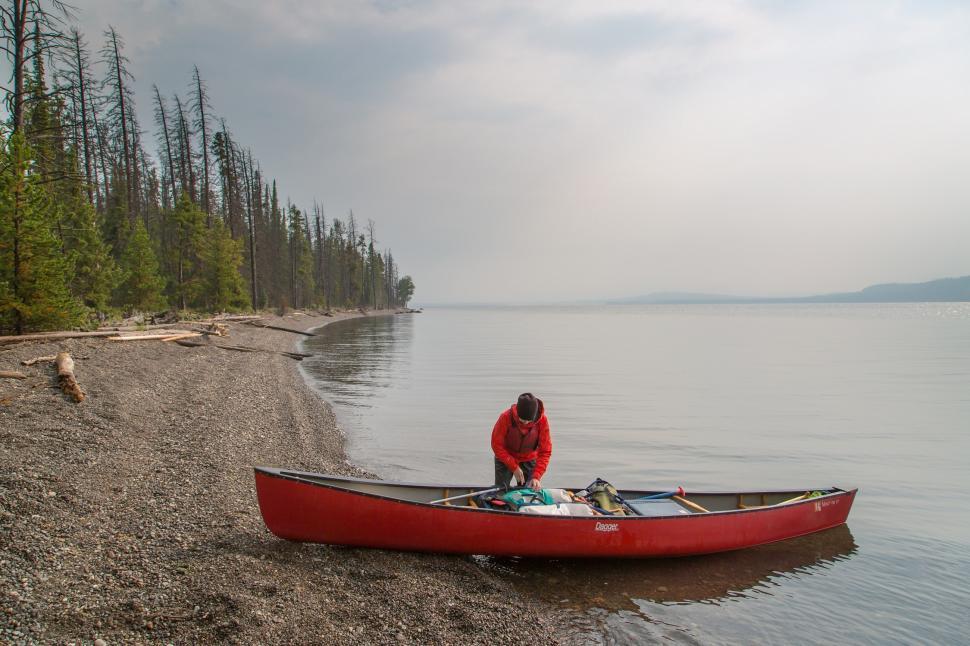 Free Image of Man Standing in Red Canoe on Lake Shore 