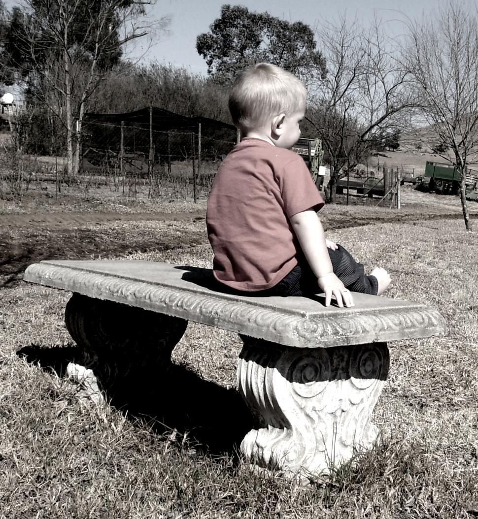 Free Image of Little Boy Sitting on Bench in Grass 