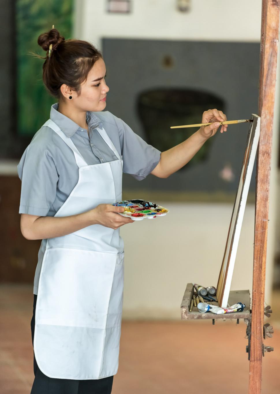 Free Image of Woman in Apron Painting on Easel 